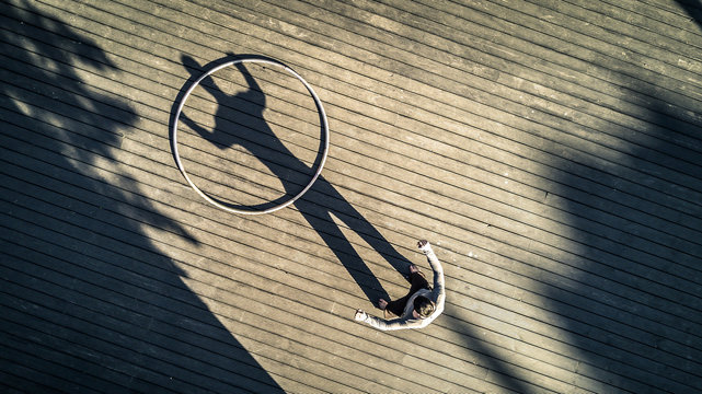 Young man is standing on the square next to the cyr wheel. On shadow looks like he is holding this wheel. Conceptual image. Sunny day.