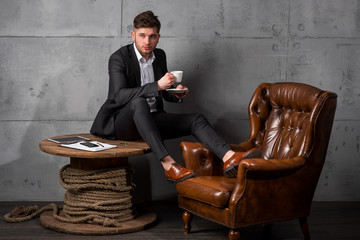 Portrait of young businessman project manager sitting in a chair on grey background loft cabinet interior copy text