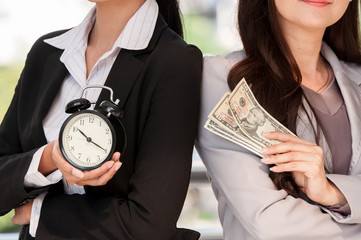 Asian businesswomen show black alarm clock and dollar bank note, business concept time to work be...