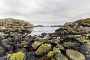 Fototapeta na wymiar Rocks covered in lichen, the ocean and islands in the background. Urd island at the Rovaer archipelago in Haugesund, norwegian west coast.