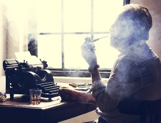 Side view of man smoking pipe while working on typewriter