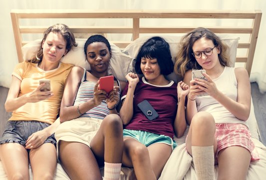 Group Of Diverse Women Lying On Bed Using Mobile Phones Together