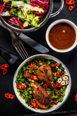 Grilled chicken drumsticks and vegetables in pan on black stone