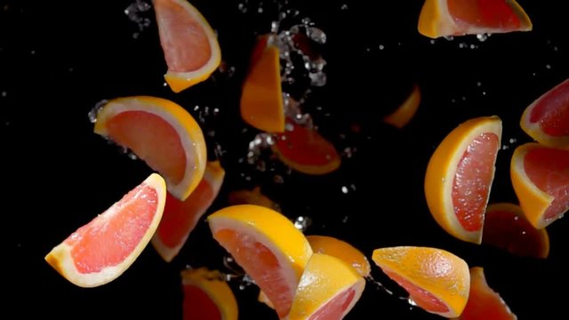 Slices of grapefruit with water bouncing against to the camera on a black background in slow motion
