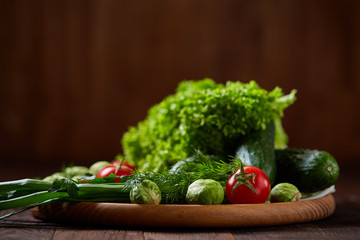 Vegetarian still life of fresh vegetables on wooden plate over rustic background, close-up, flat lay.