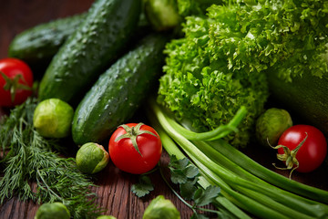 Vegetarian still life of fresh vegetables on wooden plate over rustic background, close-up, flat lay.
