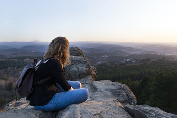 girl sits on a rock above the mountain valley and looks towards the horizon