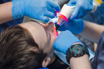 A dentist and an assistant treat the teeth of a young man. Teenager in dentistry.