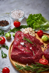 Still life of raw beef meat with vegetables on wooden plate over white background, top view, selective focus