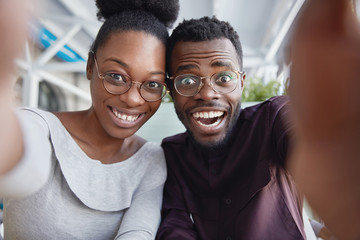 Joyful black male and female best friends have fun together, take picture of themselves or pose for making selfie, being in good mood after successful day. People, friedship, leisure, happiness