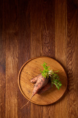 Bundle of carrots with soil on wooden plate over rustic wooden background, side view, close-up, selective focus