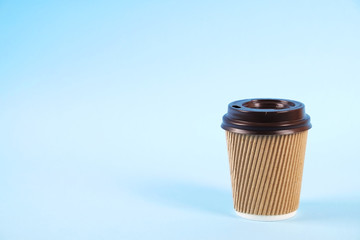 Brown disposable safe heat resistant double walled paper take out cup of coffee to go. Colorful eco-friendly cardboard mug for hot beverages, white cap on blue gradient background, close up copy space