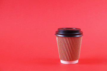 Brown disposable safe heat resistant double walled paper take out cup of coffee to go. Colorful eco-friendly cardboard mug for hot beverages, white cap on bright red background, close up copy space.