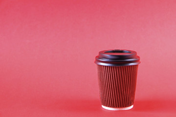 Brown disposable safe heat resistant double walled paper take out cup of coffee to go. Colorful eco-friendly cardboard mug for hot beverages, white cap on bright red background, close up copy space.