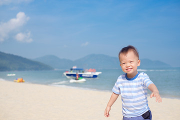 Cute happy fun little Asian 18 months, 1 years old toddler boy child running on sandy tropical sunny beach in summer vacation, Kids play at sea, Family travel concept, Batu Ferringhi, Penang, Malaysia
