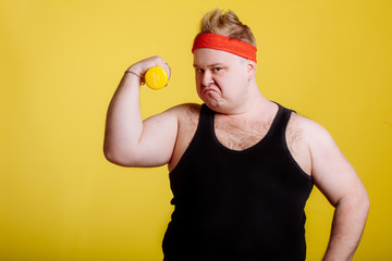 Fat man shows his muscle while holding dumbbell in hand