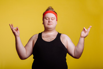 Calm fat man relaxing with meditation on yellow background