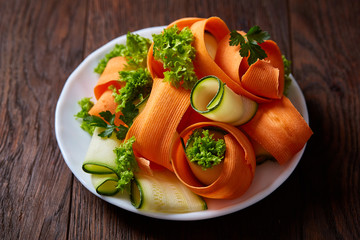 Artistically served vegetable salad with carrot, cucumber, letucce over wooden background, selective focus