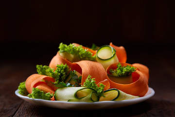 Artistically served vegetable salad with carrot, cucumber, letucce over wooden background, selective focus