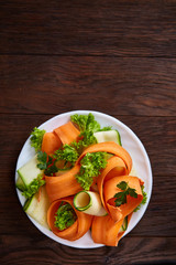 Artistically served vegetable salad with carrot, cucumber, letucce over wooden background, selective focus