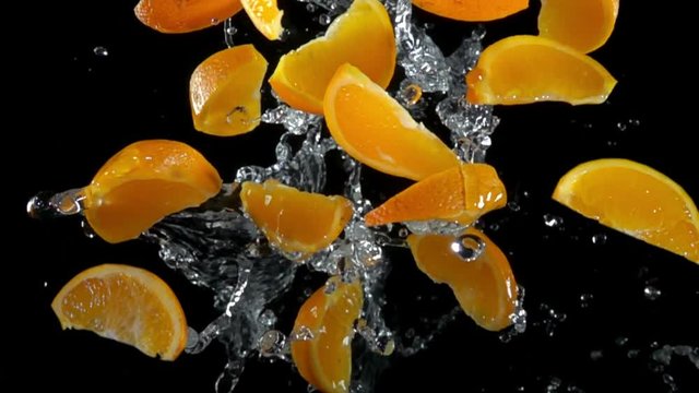 Slices of orange with water flies to the camera on a black background in slow motion