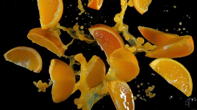 Slices of orange with juise flies to the camera on a black background in slow motion