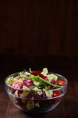 Fresh vegetable salad served in glass bowl over dark wooden background, selective focus, shallow depth of field