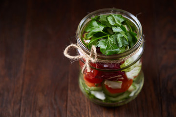 Creative vegetable salad served in glass jar over dark wooden background, selective focus, shallow depth of field
