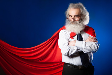 Fototapeta na wymiar Super hero in the glasses. The man is a superhero. An old man with a red cloak. Fearless man. A gray-haired man with glasses. Gray beard. Grandfather is a super hero.