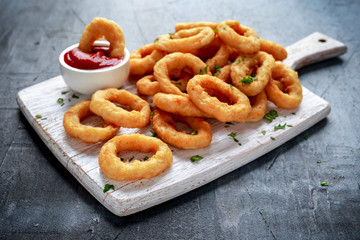 Fried Onion Rings with Ketchup on white cutting board.