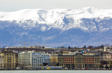 Facades of historic buildings in the city center of Geneva, Switzerland on the Leman lake with snow covered Alps mountains peaks in sunny clear day.