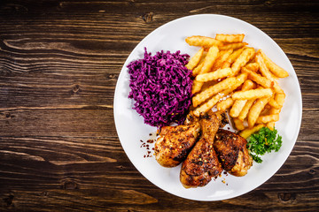 Grilled drumsticks with french fries and vegetables on wooden background