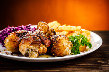 Grilled drumsticks with french fries and vegetables on wooden background