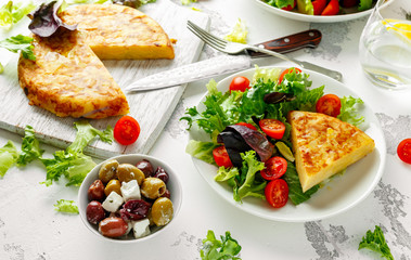 Spanish tortilla, omelette with potato, onion, vegetables, tomatoes, olives and herbs in a white plate. breakfast, healthy food.