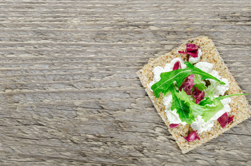 Crisp bread with soft cream cheese and herbs on a wooden table. Top view, background.