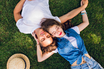 Romantic couple of young people lying on grass in park. They lay on the shoulders of each other and...