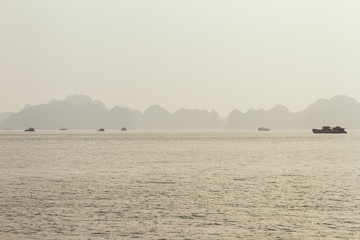 Tourists boats are cruising on the emerald waters with thousands of towering limestone islands in background in golden hour at Quang Ninh, Vietnam