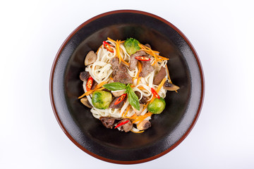 Wheat noodles with mushrooms and vegetables under teriyaki sauce, isolated on white background. Wheat noodles in a black plate.