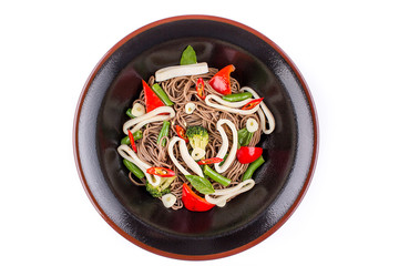 Buckwheat noodles with squid and vegetables with teriyaki sauce isolated on a white background. Buckwheat noodles in a black plate.