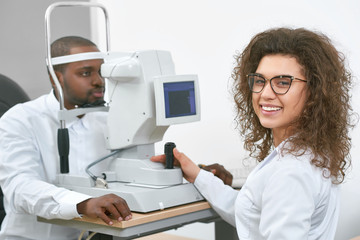 Friendly smiling doctor is checking patient's vision with special ophthalmological equipment in...