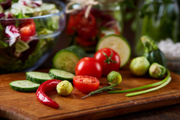 Fresh vegetable salad and ripe veggies on cutting board over wooden background, close up, selective focus