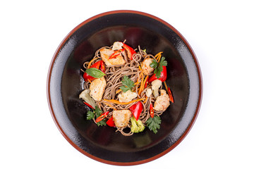 Buckwheat noodles with meat and vegetables under teriyaki sauce, isolated on white background. Buckwheat noodles in a black plate.
