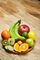 Ripe fresh fruits in a wooden plate on a light wooden background, selective focus, close-up, top view