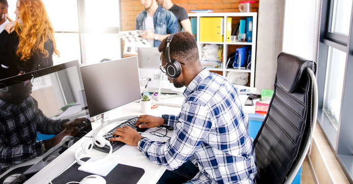 side view shot of african typist with headphones whose fingers are hammering the keys