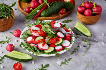 Creative fresh vegetable salad with ruccola, cucumber, tomatoes and raddish on white plate, selective focus
