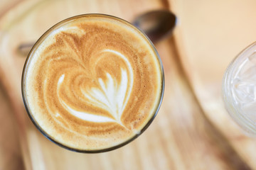 Coffee with heart-shaped cream, white cup on the glass table.
