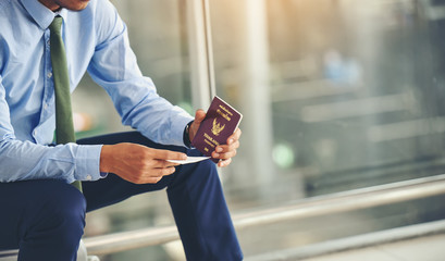 An Asian businessman is holding a plane ticket and his passport is waiting to depart.Focus on hand...