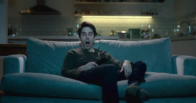 Tired and sleepy man yawning as he  watches tv late at night.