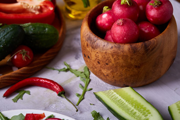 Fresh red radish in wooden bowl among plates with vegetables, herbs and spicies, top view, selective focus.