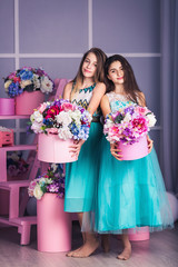Two beautiful girls in blue dresses in studio with decor of flowers in baskets.